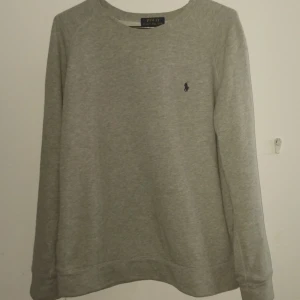 Grå sweatshirt från Polo Ralph Lauren - Säljer en stilren grå sweatshirt från Polo Ralph Lauren med klassisk broderad logga på bröstet. Tröjan har rund halsringning och långa ärmar, perfekt för en chill och enkel look. Tillverkad i mjuk bomullsmix som är skön att ha på sig.
