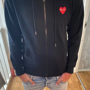 Svart hoodie Comme des Garçons Play - Svart hoodie från Comme des Garçons Play med dragkedja, huva och snörning. Storlek M men passar S. Helt oanvänd med tagg
