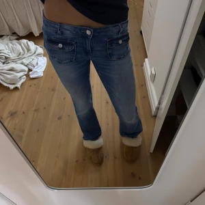 Blå bootcut jeans från Gina Tricot - Snygga blå jeans från Gina Tricot med bootcut-modell och coola fickor framtill med lock och knapp. Klassisk femficksdesign och normal passform. Jag har sprättat upp trådar längst ner för att göra jeansen längre, tycker själv att de blev såå mycket snyggare 🙌🏻 Heansne har använts ett par gånger och har en liten ”skada” vid framfickan men som inte syns eller läggs märke till 🤗