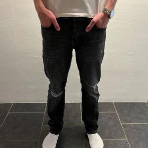 Svarta tapered jeans från Jack & Jones - W28 L32. Snygga svarta jeans från Jack & Jones med tapered fit och coola slitningar på benen. Jeansen har klassisk femficksdesign, normal passform och är gjorda i mjukt bomullsmaterial med lite stretch. Perfekta för dig som gillar en avslappnad men stilren look.