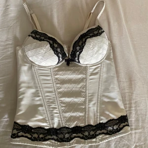  korsett - Supersnygg champagnefärgad korsett från H&M med svarta spetsdetaljer. Justerbara axelband och hakknäppning bak. Perfekt för att lyfta vilken outfit som helst.