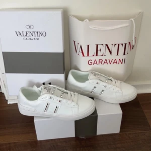 Valentino Rockstud sneakers i vitt skinn - Säljer ett par vita Valentino Garavani Rockstud Untitled sneakers med silverfärgade nitar och vit snörning. Skorna är tillverkade i skinn och har en chunky platt sula med mönster. Köpte dem i fel storlek tyvärr så vill helst bara bli av med dem nu haha. Dem är helt oanvända! Pris kan diskuteras 🩷