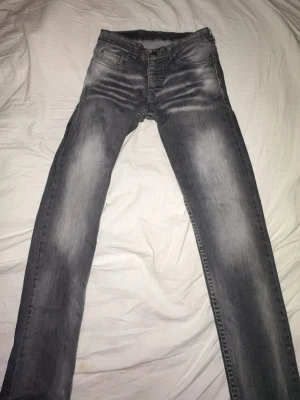 Grå Dsquared2 jeans, storlek 32 - Säljer ett par grå jeans från Dsquared2 i storlek 32. Jeansen har en snygg tvätt med slitningar och ljusare partier framtill och baktill. Klassisk femficksmodell med raka ben och normal passform. Tillverkade i 100% bomull för skön känsla.