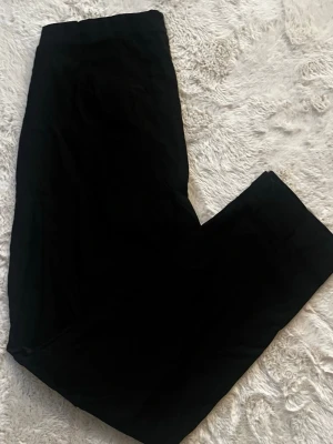 Svarta byxor från LauRie, stl 44 - Säljer ett par svarta byxor från LauRie i storlek 44. Byxorna har rak passform och är tillverkade i ett mjukt bomullsmaterial. Klassisk look med diskret logga på bakfickan. Perfekta till en clean och enkel outfit.