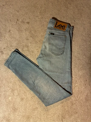 Lee Malone ljusblå skinny jeans W28 L32 - Snygga ljusblå jeans från Lee, modell Malone. Jeansen har en skinny passform och klassisk femficksdesign med Lee-logga på bakfickan. Tillverkade i mjukt denimtyg som sitter tajt hela vägen ner.