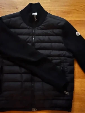 Svart pufferjacka från Moncler - Säljer en svart pufferjacka från Moncler med quiltad front och stickade ärmar. Jackan har dragkedja framtill, ribbad krage och två sidofickor med dragkedja. Klassisk Moncler-logga på ärmen och stilren design som funkar till allt. Skick 9/10 skriv gärna vid intresse. Finns även i M