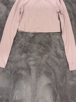 Ljusrosa croppad långärmad topp H&M - Säljer en ljusrosa croppad långärmad topp från H&M. Toppen har enkel design med rund halsringning och är tillverkad i mjuk bomull. Perfekt att styla med höga jeans eller kjol för en clean look.