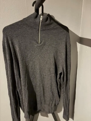 Mörkgrå half zip tröja Jack & Jones - Mörkgrå långärmad tröja från Jack & Jones med ribbad krage och half zip-dragkedja. Tröjan har en clean look och är tillverkad i mjukt material som känns skönt mot huden. Perfekt till jeans eller chinos för en chill och stilren vibe.