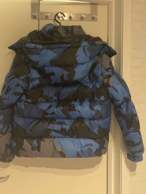 Blå och svart pufferjacka Moncler - Säljer en fet pufferjacka från Moncler med blått och svart camomönster. Jackan är i storlek 1 som är ungefär xs skulle ja säga passar mig som är 178 och väger 65 kg lite liten men funkar ändå. Jackan har huva, dragkedja och är riktigt vadderad för max värme. Insidan är svart och glansig med Moncler-etikett och serietidningsdetalj. Perfekt för kalla dagar när du vill sticka ut. pris diskuteras vid snabba affärer 