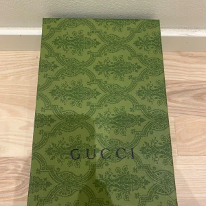 Gucci keps med GG-mönster - Snygg beige keps från Gucci med klassiskt GG-monogram i brunt över hela kepsen. På sidan finns den ikoniska gröna och röda randen. Kepsen har böjd skärm och justerbar rem bak. Perfekt för dig som vill ha en lyxig streetstyle-look. Du får boxen med.