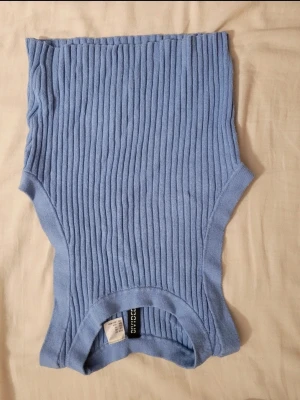 Ljusblå ribbad ärmlös topp  - Säljer en ljusblå ribbad topp från H&M. Toppen är ärmlös och har en croppad passform med breda axelband. Materialet är mjukt och stretchigt, perfekt för varma dagar eller som layering-piece.