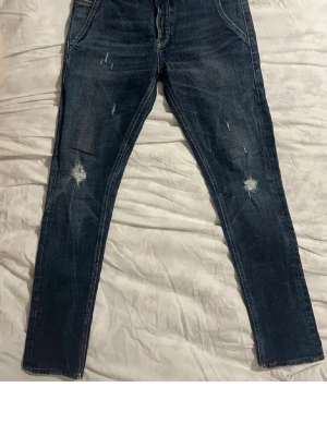 Mörkblå Dondup Jeans - Säljer ett par mörkblå jeans från Dondup med snygga slitningar på benen och klassiska kontrastsömmar. Jeansen har fem fickor, normal passform. Materialet är tåligt jeans-tyg i bomull. Perfekta för dig som gillar en avslappnad och trendig look. De sitter som Dondup georg. Längd: 95cm