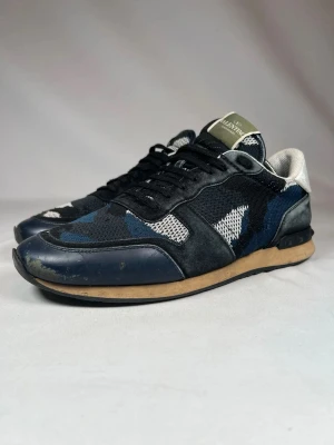 Valentino Garavani camo sneakers - (Nypris 6200kr)Snygga sneakers från Valentino Garavani med svart, blå och vit camouflagemönstrad ovandel i mesh och mocka. Skorna har svarta snören, beige sula och detaljer i skinn. Perfekta för dig som vill ha en unik och trendig look.