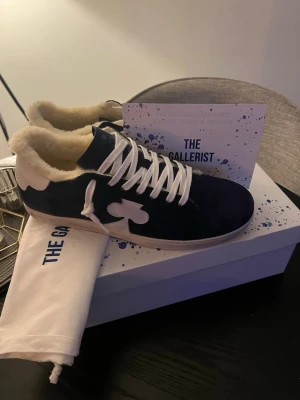 The gallerist  - Snygga marinblå sneakers med vit fuskpälsfoder och vita detaljer. Skorna har vit snörning och en unik vit klubb-symbol på sidan. Ovandelen är i mocka och insidan är fodrad för extra värme. Perfekta för dig som vill sticka ut med en cool och mysig stil. Nypris 2700kr