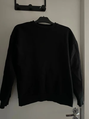 Svart sweatshirt från NA-KD - En basic svart sweatshirt från NA-KD i storlek XXS. Tröjan har rund halsringning, ribbade muddar vid ärmslut och nederkant samt en loose passform. Perfekt till chill dagar eller när du vill ha en enkel och clean look.