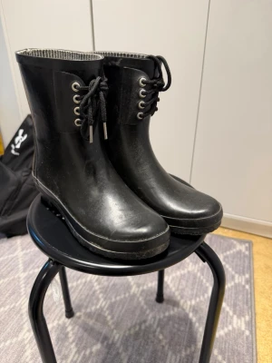 Svarta gummistövlar - Säljer ett par svarta gummistövlar med snörning och rund tå. Insidan har ett randigt foder i svart och vitt. Perfekta för regniga dagar och har en klassisk, enkel look som funkar till det mesta.