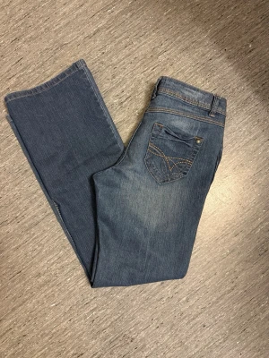 Blå bootcut jeans med broderade fickor - Säljer ett par klassiska blå bootcut jeans med snygga broderade detaljer på bakfickorna och kontrastsömmar. Jeansen har normal passform, fem fickor och är tillverkade i mjukt denimtyg. Skriv för mer information, pris går att diskuteras. 💗