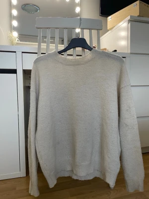 Beige stickad tröja från Gina Tricot - Mysig beige stickad tröja från Gina Tricot i oversized modell. Tröjan har rund halsringning, ribbade muddar och långa ärmar. Perfekt för lager på lager under höst och vinter. Enkel och stilren design som passar till allt.