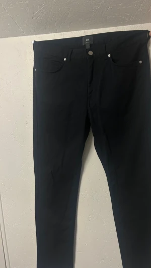 Jeans - Säljer ett par svarta slim fit byxor från H&M i storlek 33/30. Byxorna har klassisk femficksdesign, silverfärgade nitar och knapp, samt smal passform. Materialet är mjukt och stretchigt, vilket gör dem riktigt bekväma att bära.