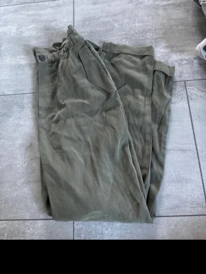 Olivgröna cargopants med fickor - Säljer ett par olivgröna cargopants med klassiska sidofickor och knapp i midjan. Byxorna har en avslappnad passform och är perfekta för en chill och casual stil. Tillverkade i mjukt bomullsmaterial för extra komfort.