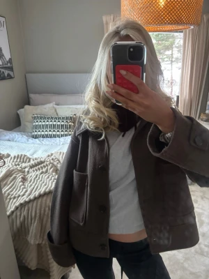 Brun kort kappa - Säljer en brun kappa med stora framfickor och bred krage. Jackan har knäppning med stora knappar och en rak, lite boxig passform. Perfekt för dig som gillar en enkel men snygg look.