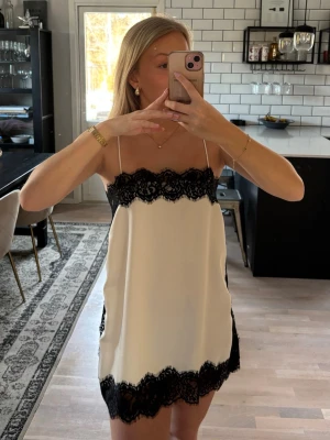 Vit satinklänning/topp med svarta spetsdetaljer - Zara - Supersnygg vit satinklänning/topp från Zara med tunna axelband och breda svarta spetsdetaljer upptill och nedtill. Öppning i sidorna nedtill. Snygg både som kortklänning och längre topp. Helt slutsåld på Zaras hemsida. Klänningen är helt oanvänd med prislappen kvar. Jag är 163 cm lång. Publicerad på flera säljsidor. 