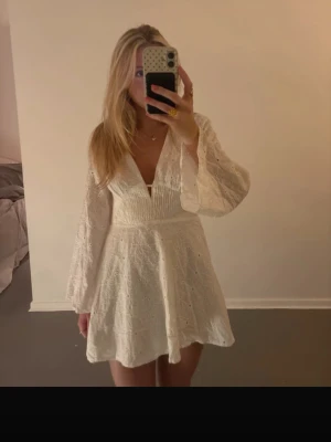 Studentklänning - Supersöt vit kortklänning från NA-KD med broderade blommor, v-ringning och vida långärmar. Klänningen har öppen rygg och är perfekt för sommar eller student! Lånade bilder!!