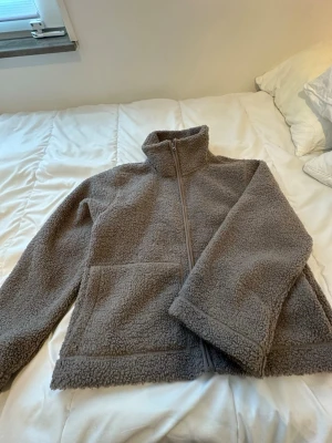 Beige teddyjacka med dragkedja - Mysig beige teddyjacka med hög krage och hel dragkedja framtill. Jackan har två stora fickor och är tillverkad i fluffigt teddy-material som håller dig varm. Perfekt för kyliga dagar och enkel att matcha med olika outfits.