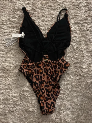Leopardmönstrad baddräkt - Säljer en snygg leopardmönstrad baddräkt med smala svarta axelband och en cool ringdetalj i ryggen. I storlek XS. Från New Yorker. Baddräkten har djup v-ringning. Perfekt för dig som vill sticka ut på stranden. Gåva vid köp!🎁