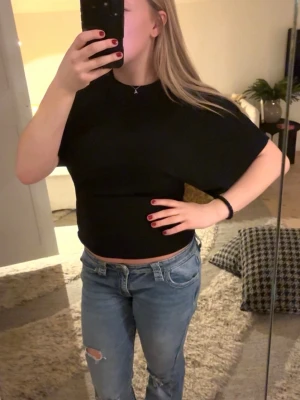 Svart croppad topp med kort ärm - Säljer en svart croppad topp med korta utsvänga armar och rund halsringning. Enkel och stilren design som passar till mycket. Köptes på Nelly och är i bra skick. 