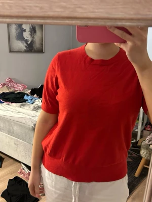 Röd stickad topp med kort ärm - En enkel och snygg röd stickad topp med rund halsringning och korta ärmar. Modellen är rak och passar perfekt till både jeans och kjol. Mjuk och skön känsla, perfekt för dig som gillar färg.