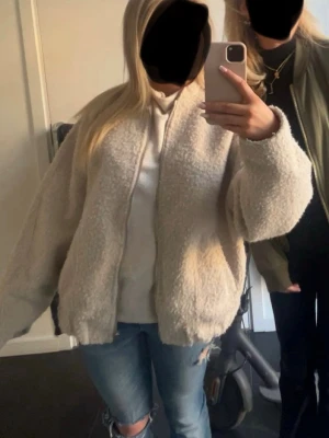 Stickad bomberjacka  - Mysig beige teddyjacka med dragkedja framtill och avslappnad passform. Jackan har en fluffig struktur och är perfekt för kyligare dagar. Passar dig som gillar en oversized look och vill ha något både snyggt och bekvämt.