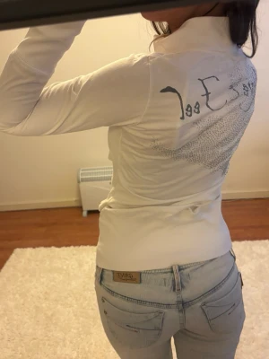Vit ziptröja med strass och text - Säljer en vit ziptröja med lång ärm, hög krage och dragkedja framtill. Baksidan har text och strassdetaljer. Jag är 168 och det är mina bilder, köp via köp nu direkt eller Swish, kvar tills markerad som såld 💖 vissa strass har ramlat av , men det syns inte mkt. 