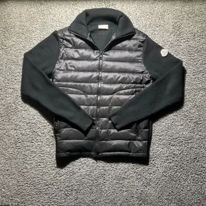 Svart Moncler cardigan - Snygg svart cardigan från Moncler med stickade ärmar och krage. Inga defekter eller liknande den är i storlek m men sitter som en s hör av er vid frågor eller funderingar!