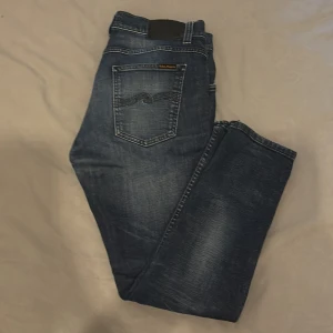 Nudie jeans - Snygga mörkblå jeans från Nudie Jeans, tight terry med klassisk femficksdesign och diskreta slitningar. Jeansen har kontrastsömmar samt Nudie-logga på bakfickan. Perfekta för dig som gillar en stilren och tidlös look.