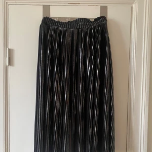 Plisserad svart metallic långkjol från Ivyrevel - Säljer en plisserad lång/midikjol från Ivyrevel i svart med metallicglans. Kjolen har resår i midjan och skimrande effekt.