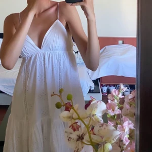 Vit somrig klänning från Zara - Superfin vit kort klänning från Zara med tunna axelband och v-ringning. Klänningen har broderade detaljer och volang nertill, perfekt för varma dagar. Tillverkad i bomull och har en luftig passform som känns riktigt fräsch och lätt.