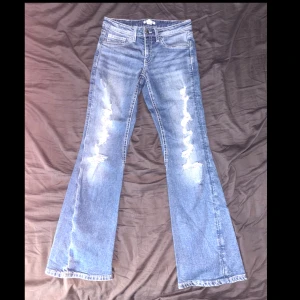 Bootcut jeans från Gina Tricot - Snygga blå bootcut jeans från Gina Tricot med slitna detaljer framtill. Jeansen har klassisk femficksdesign, låg midja och är tillverkade i bomull med lite stretch. Perfekta för dig som gillar en retro och avslappnad look.  • Midja 38,2cm  • Total längd från midja till ben öppningen 99cm  • Benöppningen bredd 24cm