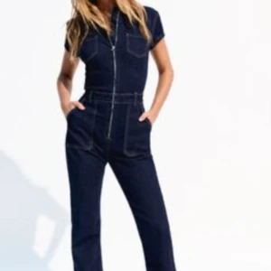 Mörkblå jeans jumpsuit med dragkedja - Snygg mörkblå jeans jumpsuit med korta ärmar, markerade sömmar och stora fickor framtill. Dragkedja både vid bröstet och i midjan