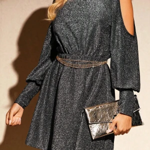 Glittrig svart kortklänning med kedjebälte - Supersnygg svart glittrig kortklänning med markerad midja och kedjebälte. Klänningen har långa ärmar med öppna axlar och en lätt utställd kjol. Perfekt för dig som vill sticka ut med stilren glamour.