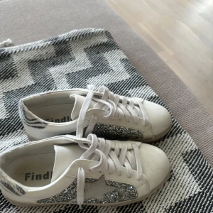 Vita sneakers med silverglitter - Snygga vita sneakers från Findlay med silverglittriga detaljer och stjärna på sidan. Skorna har vita snören, rund tå och platt sula. Baksidan har zebramönstrade detaljer! skit snygga! pris går givetvis att diskutera ! nypris 1200💝💝💝