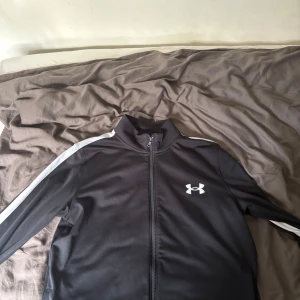 Svart träningsjacka från Under Armour - Snygg under armour tröja, tröjan är perfekt för träning eller om du vill ha en stilig outfit.