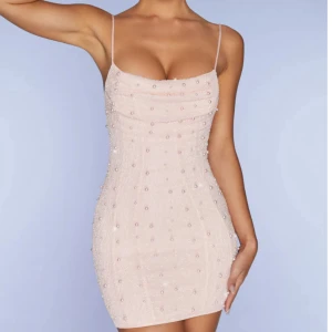 Ljusrosa pärlprydd kort klänning - Superfin ljusrosa kort klänning med tunna axelband, öppen rygg och knyt i ryggen. Klänningen är täckt av små pärlor och har en draperad urringning. Bara använd ett fåtal gånger. Storlek uk 4/xxs, men skulle säga den passar en xs också. 84% polyester 16% elastane. Mått finns på sista bilden. Pris går att prutas.