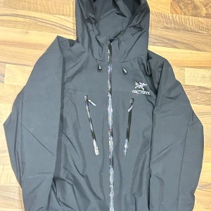 Arc'teryx windbreaker - Svart vindjacka från Arc'teryx med huva och flera vattentäta dragkedjor framtill. Justerbara snören vid huvan och midjan. Perfekt inför hösten. Pris kan diskuteras vid snabb affär.