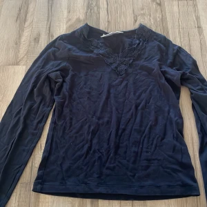 Mörkblå långärmad topp med spets - Mörkblå långärmad topp från Gina Tricot med snygg v-ringning dekorerad med spetsdetaljer. Toppens material är mjukt och stretchigt, perfekt för en stilren look. Passar dig som gillar enkla men fina detaljer.