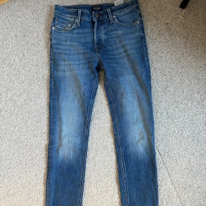 Blå jeans från Jack & Jones - Säljer ett par klassiska blå jeans från Jack & Jones med snygg tvätt och femficksdesign. Jeansen har raka ben, normal passform och detaljerade bakfickor med broderi. Perfekta för dig som gillar en tidlös stil och vill ha ett par jeans som funkar till allt. 