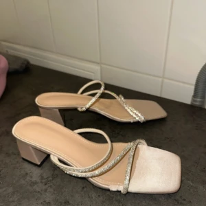 Beiga sandaler med glittriga remmar - Snygga beiga sandaler med fyrkantig tå och låg klack. Skorna har tunna remmar, varav två är dekorerade med glittrande stenar för extra bling. Perfekta för att lyfta vilken outfit som helst. Bekväm plattformsula och öppen tå ger en trendig look. Passar även storlek 39