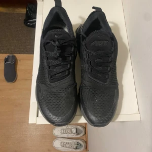 Nike Air Max 270 helsvarta sneakers - Säljer ett par helsvarta Nike Air Max 270 sneakers i storlek 44.5. Skorna har en luftig mesh-ovandel, tydlig Air Max-dämpning i hälen och klassisk Nike-logga på sidan. Snygg sportig look med snörning och platt sula, perfekta för dig som gillar streetstyle.