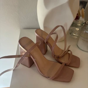 Beiga/rosa sandaler med blockklack - Snygga sandaler i beige från London Rebel med höga blockklackar och tunna remmar. Skorna har fyrkantig tå och justerbart spänne vid ankeln. Tillverkade i syntetmaterial med glansig finish, perfekta för att lyfta din outfit.