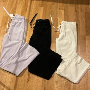 Mjukisbyxor i vitt, svart och lila - Tre par mjukisbyxor från Gina Tricot i olika färger: ett par vita, ett par svarta och ett par ljuslila. Alla har bred resår i midjan och snörning med breda band. Perfekta för chill dagar eller när du vill vara extra bekväm. 60kr st eller alla för 140kr